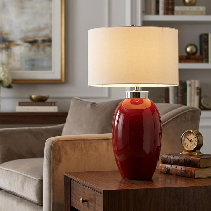 Victor Small Red Ceramic Table Lamp with a white drum shade on a wooden side table in a living room.