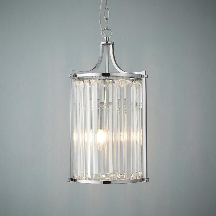 Cylindrical chrome pendant light with vertical crystal glass prisms and a lit bulb against a neutral wall.