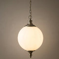 Illuminated Vulcan 1 Light brass pendant with a glowing opal glass spherical shade against a plain wall.
