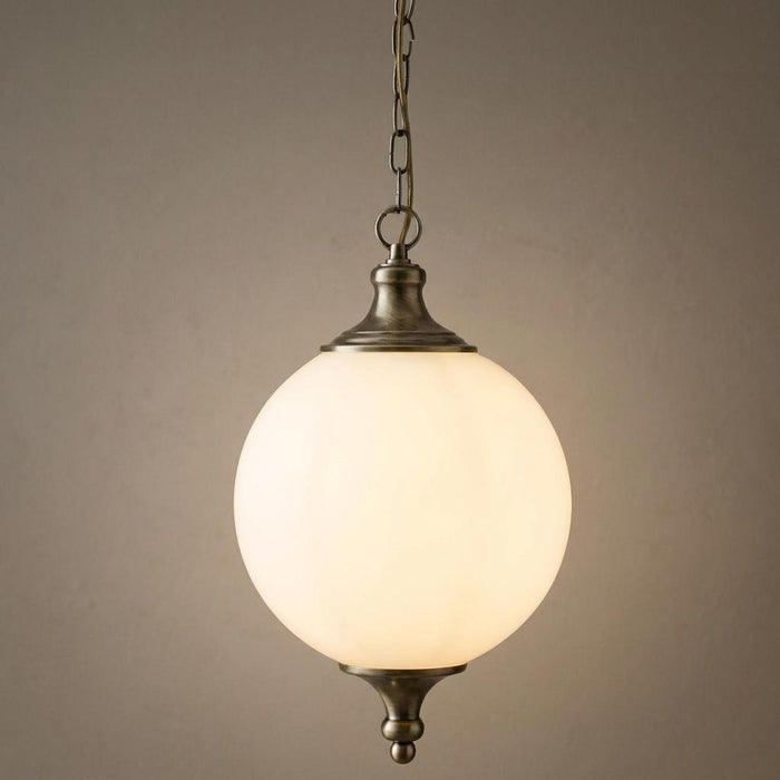 Illuminated Vulcan 1 Light brass pendant with a glowing opal glass spherical shade against a plain wall.