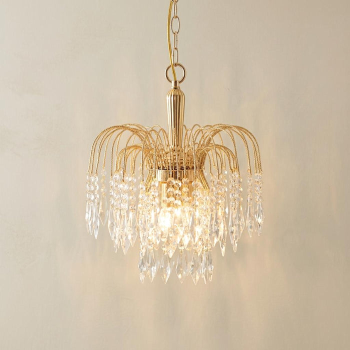 Waterfall 3-light gold and clear crystal ceiling pendant with lit bulbs against a neutral wall.