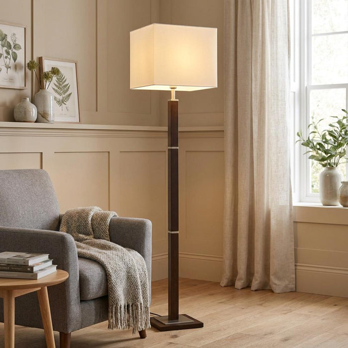 A Waverley dark wood floor lamp with a square cream shade beside a grey armchair in a neutral-toned living room.