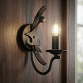 Graphite Windsor wall light with ornate metalwork and a glowing candle bulb on a dark wood surface.
