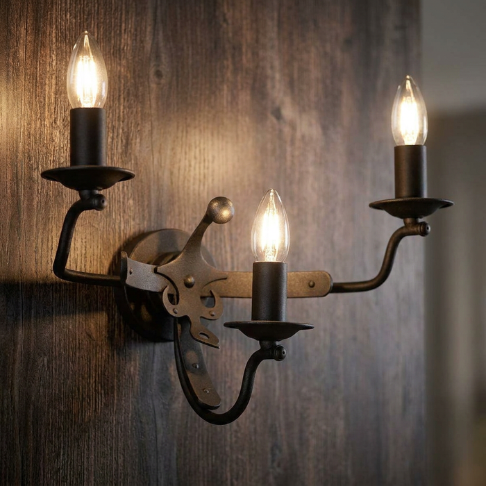 Windsor 3-light graphite wall light with medieval-style detailing on a dark wood wall.