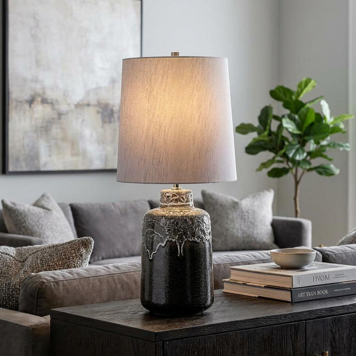 Graphite and white glazed ceramic table lamp with a grey shade on a dark side table in a modern living room.