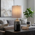 Graphite and white glazed ceramic table lamp with a grey shade on a dark side table in a modern living room.