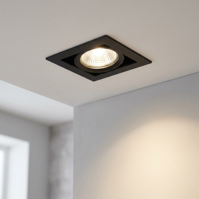Square black recessed tilt ceiling light illuminated on a white ceiling.