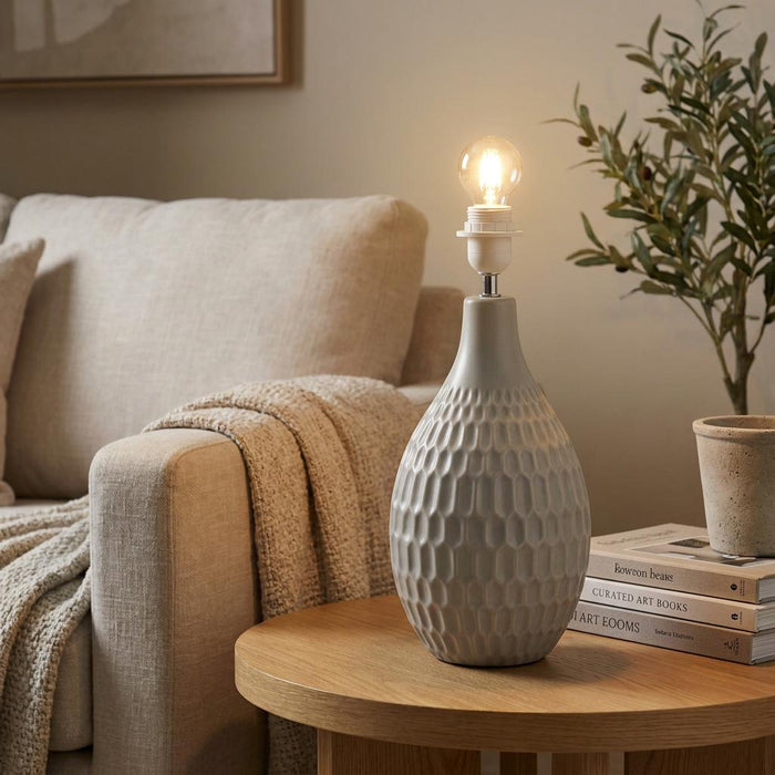 Textured grey ceramic table lamp base on a wooden side table with a lit bulb in a living room setting.