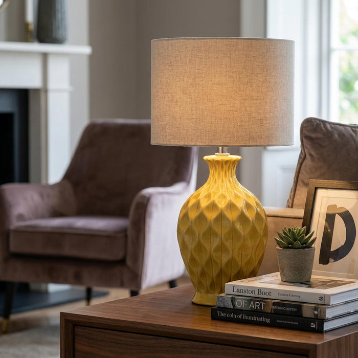 Textured yellow ceramic table lamp with a beige linen shade on a wooden side table in a living room.