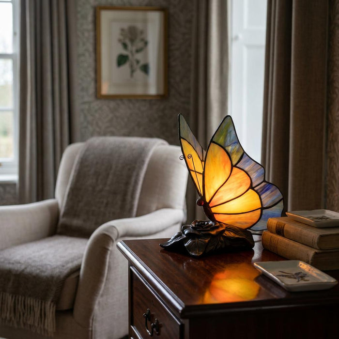 Yellow butterfly Tiffany table lamp lit on a dark wood cabinet in a cozy, neutral-toned room.