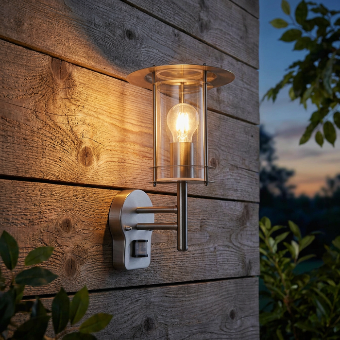 A York silver outdoor wall lantern with PIR sensor illuminated on a rustic wooden wall at dusk.