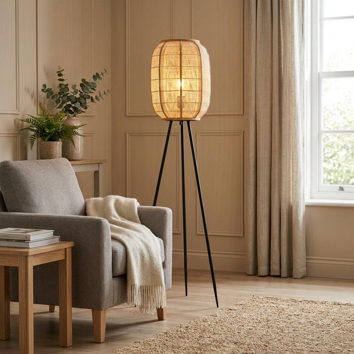 Zaire Black Floor Lamp with a glowing natural linen shade and tripod legs in a cozy living room setting.