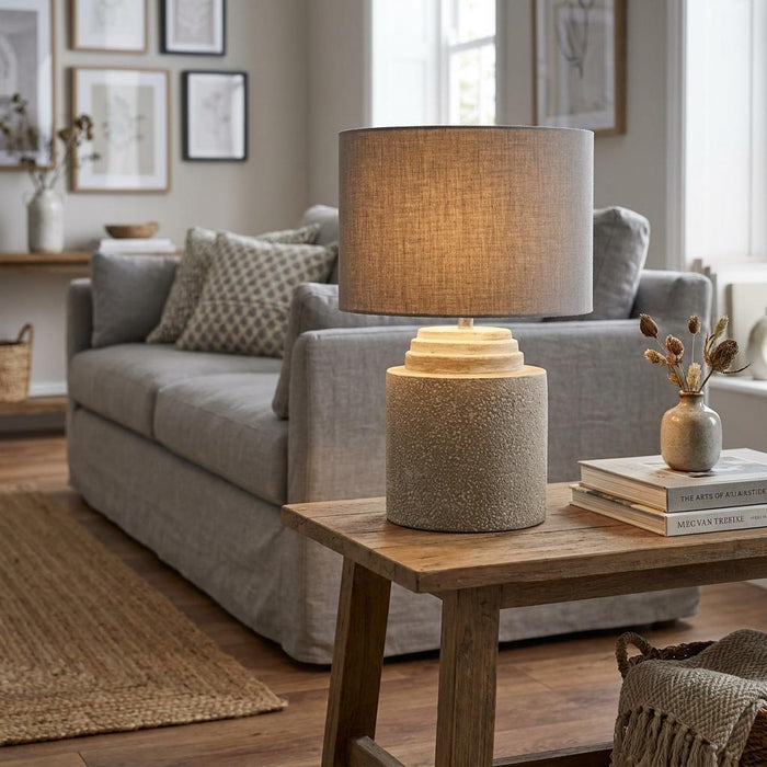 Modern grey cement table lamp with a grey linen shade on a wooden side table in a neutral living room.