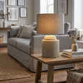 Modern grey cement table lamp with a grey linen shade on a wooden side table in a neutral living room.
